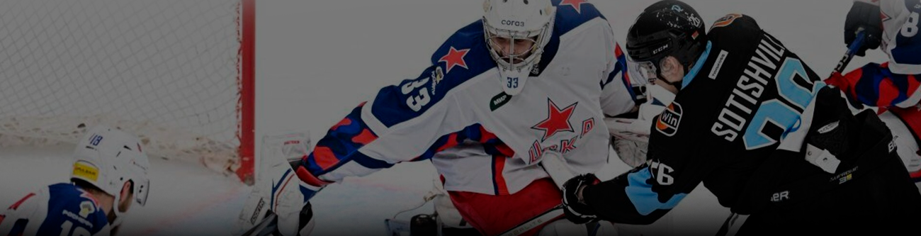 На изображении хоккейный матч: игрок в белой форме с красно-синими звездами защищает ворота от соперника в чёрной форме. Интенсивное сражение на льду