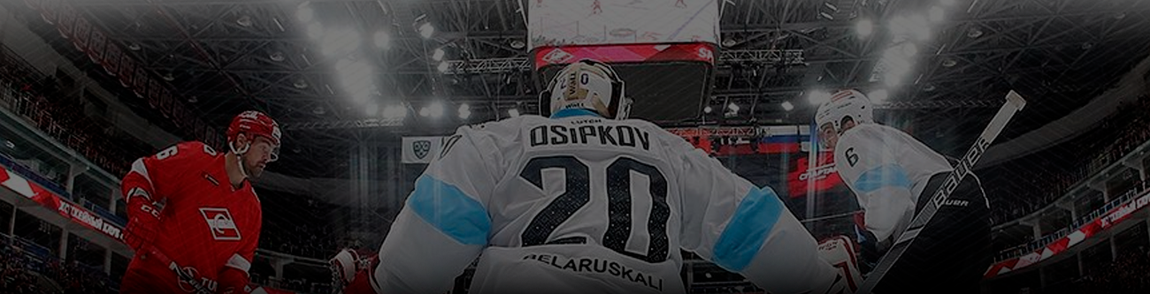 Хоккейный матч: вратарь в форме с номером 20 защищает ворота. На льду соперничают две команды, один из игроков в красной форме. Яркое освещение арены, видна часть трибун и крыши