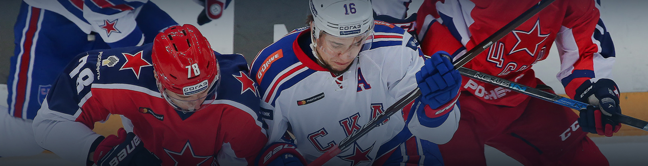 Хоккейный матч: игроки в форме с логотипами ЦСКА и СКА ведут борьбу за шайбу. Игрок в белой форме пытается овладеть шайбой, в то время как противник в красной форме ему препятствует. На льду напряженная игра