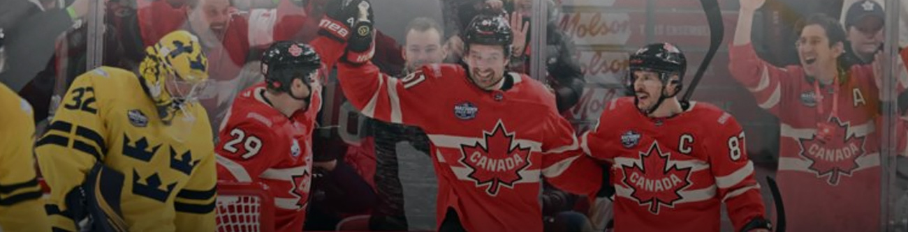 Хоккеисты в красной форме с надписью Canada празднуют событие на льду. Один игрок в жёлто-синей форме рядом. Два игрока высоко подняли руки, выражая радость. Позади видны болельщики и прозрачные борта