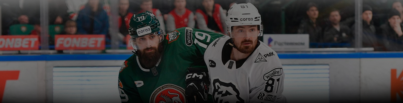 Два хоккеиста в игровой борьбе на льду. Один в зелёной форме, другой в бело-чёрной. На заднем плане видны зрители и реклама на бортике